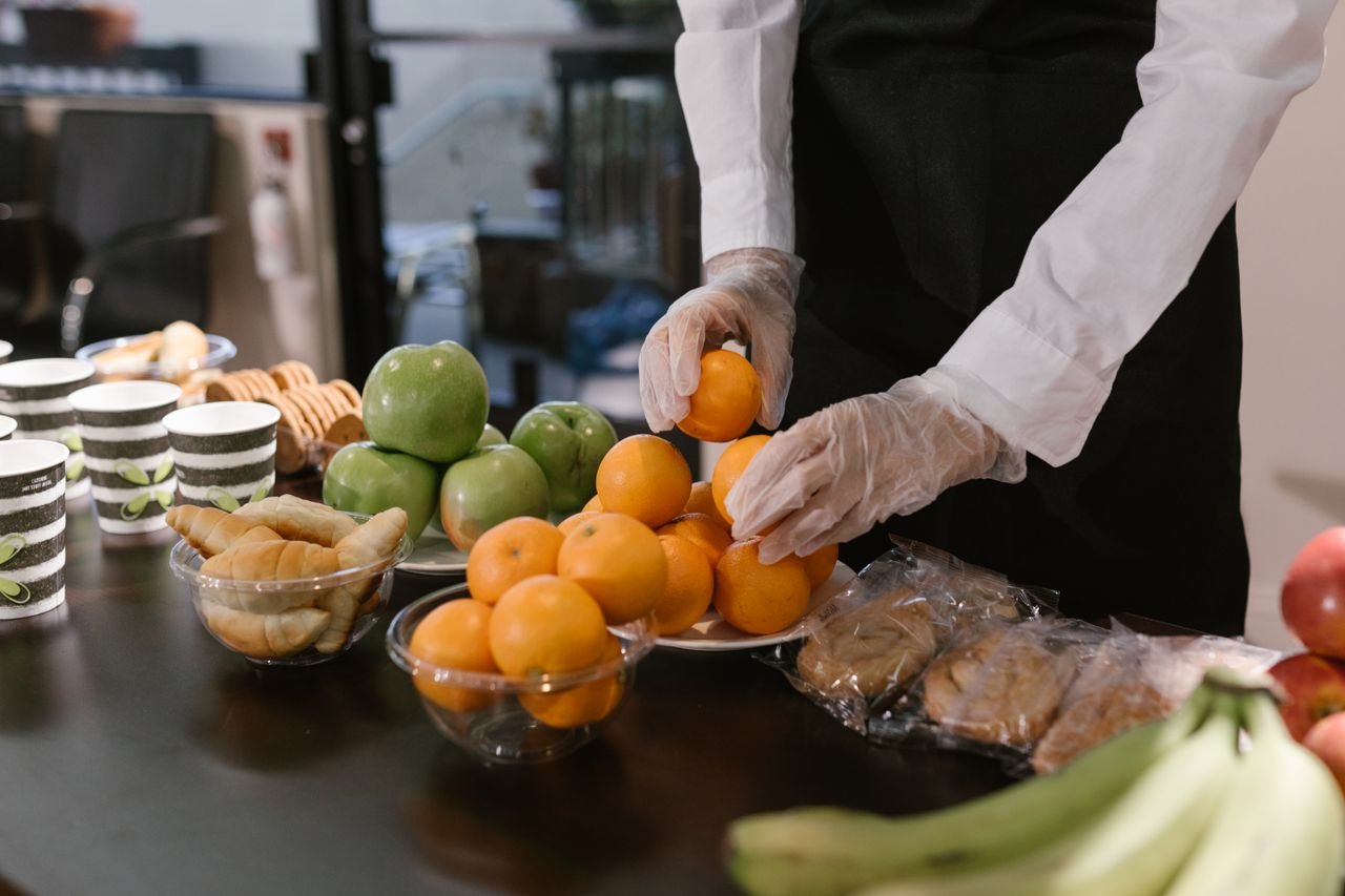 Caterer arranging fresh fruits and snacks on a table for a food service event.